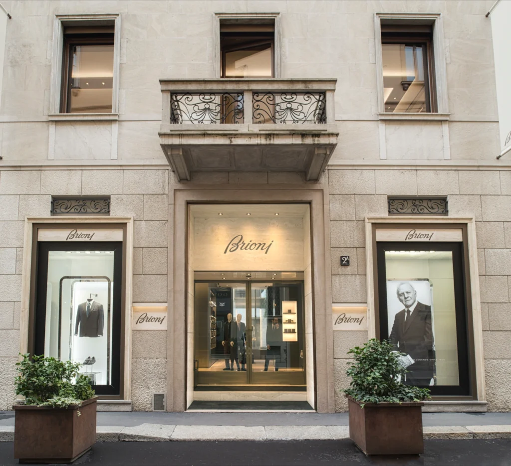 Storefront displays mannequins wearing suits, surrounded by elegant exterior design. Text reads "Brioni."