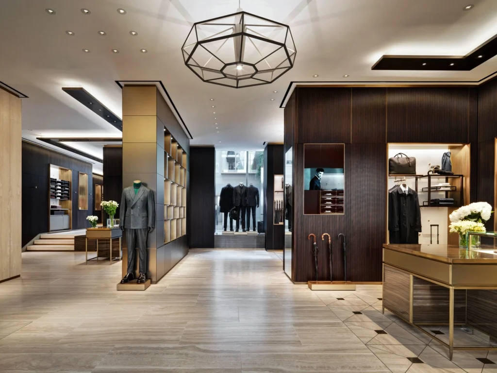 Mannequin displays suit in upscale clothing store. Umbrellas and accessories arranged neatly. Elegant interior with wood accents and lighting fixtures.