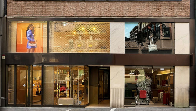 Storefront displays bags and accessories; mannequins are showcased inside; a model advertises products outside.