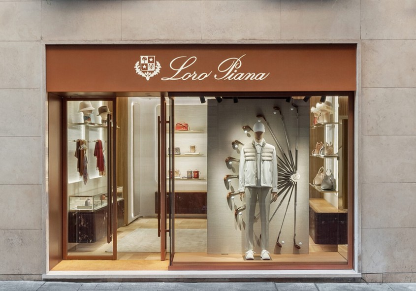 Mannequin displaying white outfit in a luxury store window; shelves show hats and bags. Sign reads: "Loro Piana."