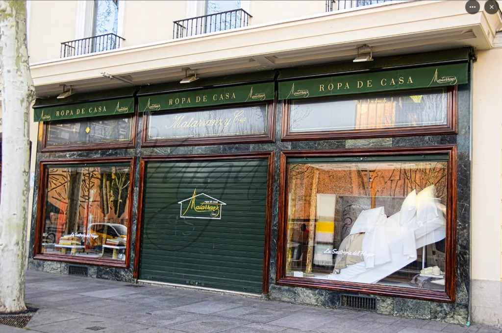 Storefront displays home textiles, showcasing bedding through large windows, in an urban setting.